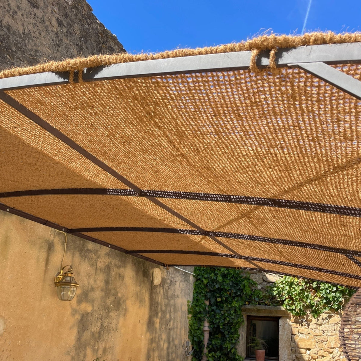 Kokos schaduwdoek met natuurlijk touw langs de rand boven een pergola
